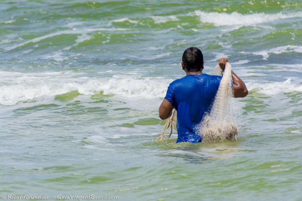 Imagem de um pescador com sua rede de pesca nas águas da Praia de Caraiva.